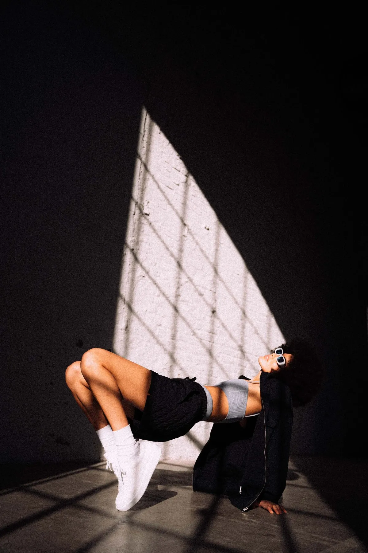Copenhagen Studios, model in black shorts and white sneakers balancing in a shaft of light with lattice shadows, campaign February 2021, photographed by Kilian Amrehn