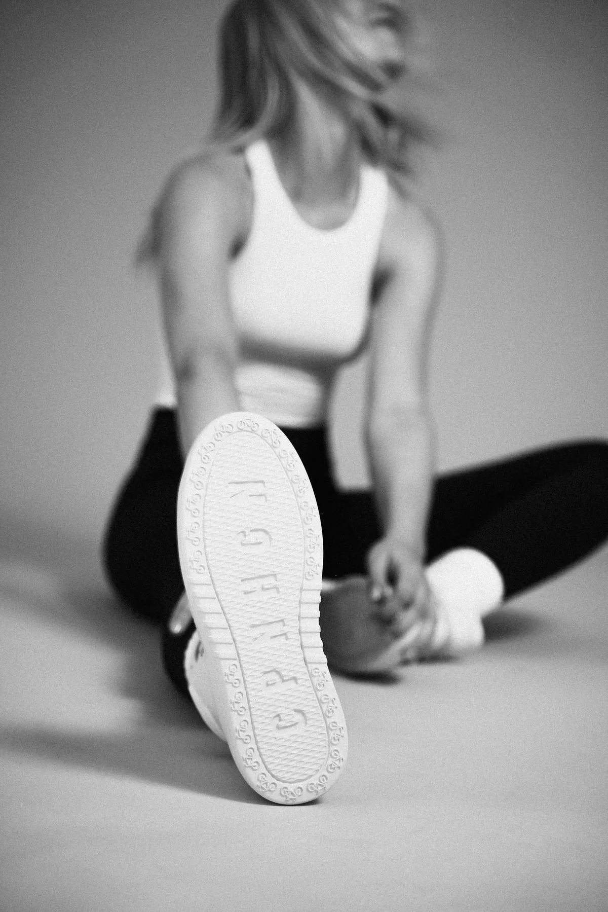 Copenhagen Studios, seated model pushing the branded sole of a white sneaker toward the camera, black and white, campaign June 2021, photographed by Kilian Amrehn