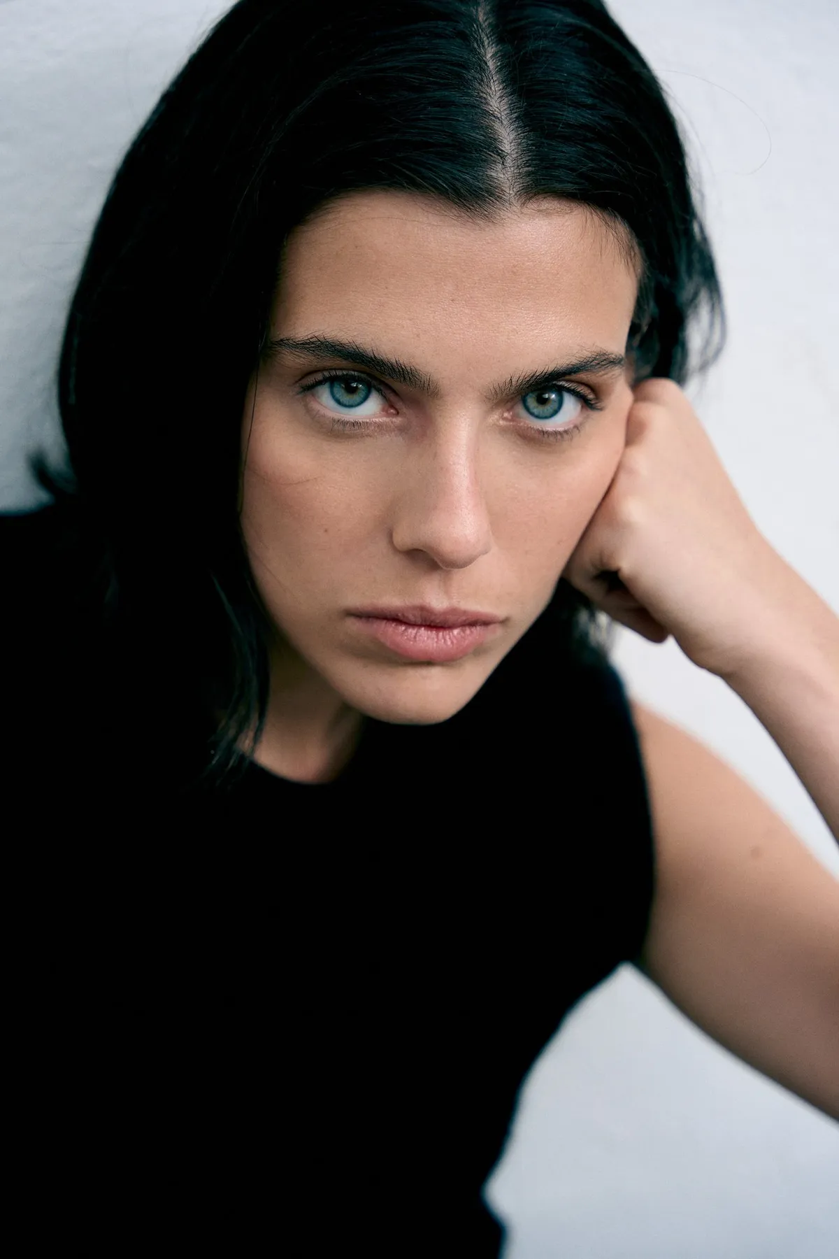 Copenhagen Studios, close portrait of a dark-haired model with pale eyes in a black top, head resting on hand, campaign October 2022, photographed by Kilian Amrehn