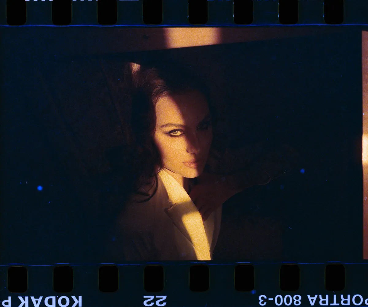 Marie, portrait of a dark-haired woman in a warm strip of light, analogue film border with sprocket holes, portrait series 2022, photographed by Kilian Amrehn