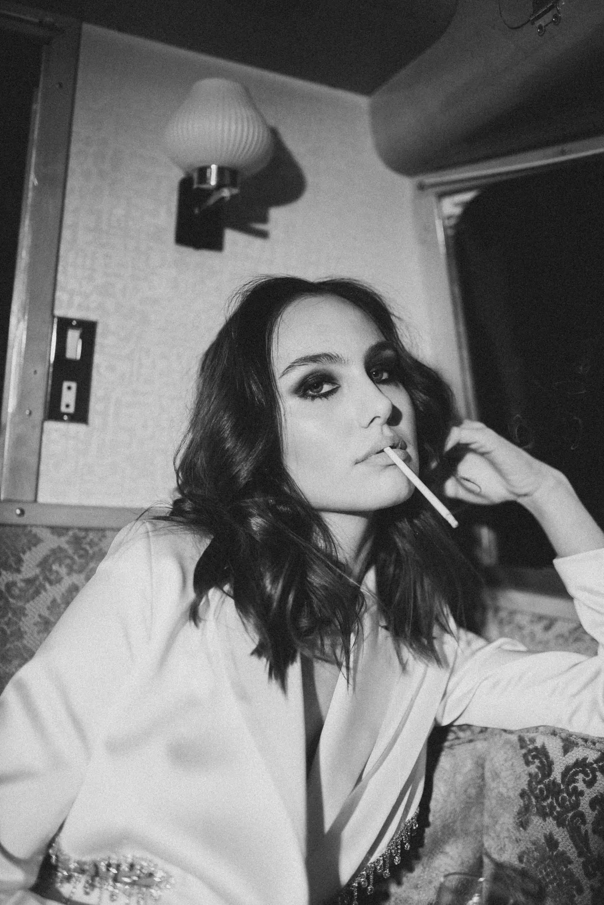 Marie, woman with smoky eyes in a white blazer smoking in a retro train compartment, black and white, portrait series 2022, photographed by Kilian Amrehn