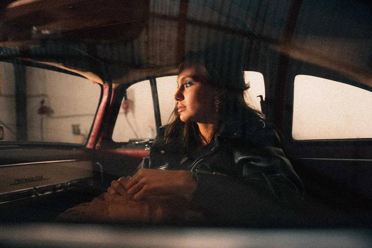 Marie, woman in a leather jacket sitting in a vintage car gazing out of the window, warm evening light, portrait series 2022, photographed by Kilian Amrehn