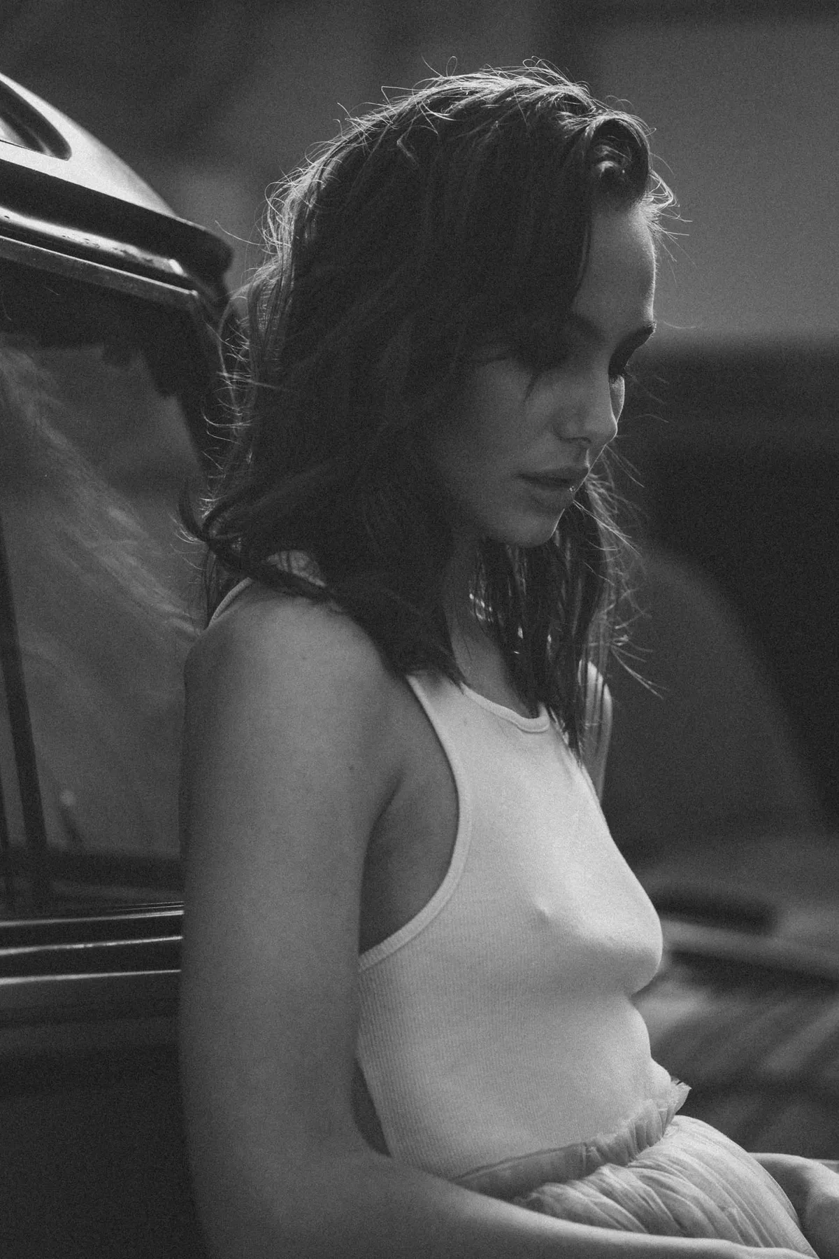 Marie, woman in a white tank top leaning on a vintage car with eyes lowered, soft backlight in black and white, portrait series 2022, photographed by Kilian Amrehn