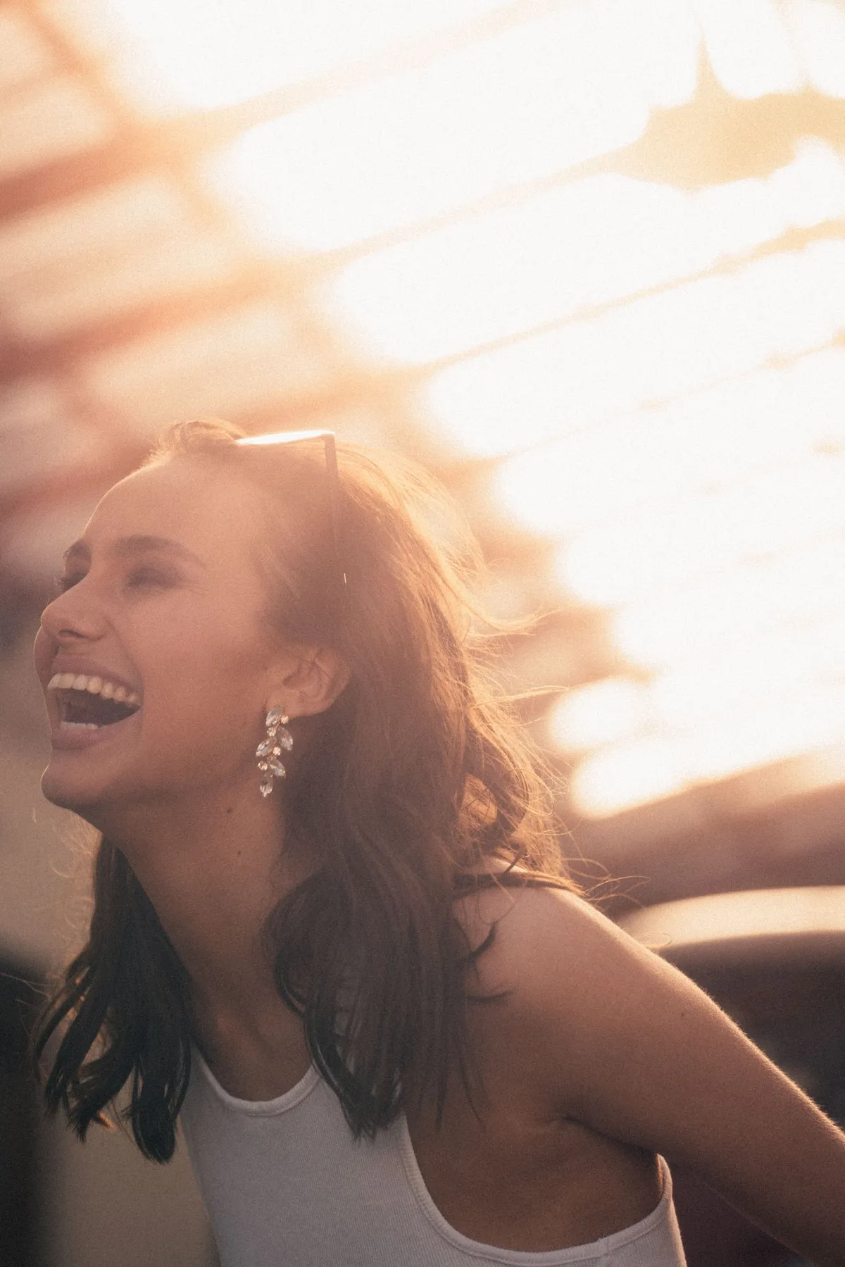 Marie, laughing woman with drop earrings and a white top in golden backlight, portrait series 2022, photographed by Kilian Amrehn