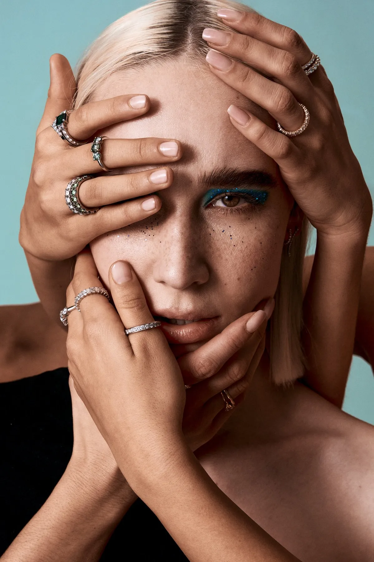 Monano, mehrere Hände mit Silber- und Edelsteinringen umrahmen das Gesicht eines Models mit blauem Lidschatten, Schmuckkampagne 2024, fotografiert von Kilian Amrehn