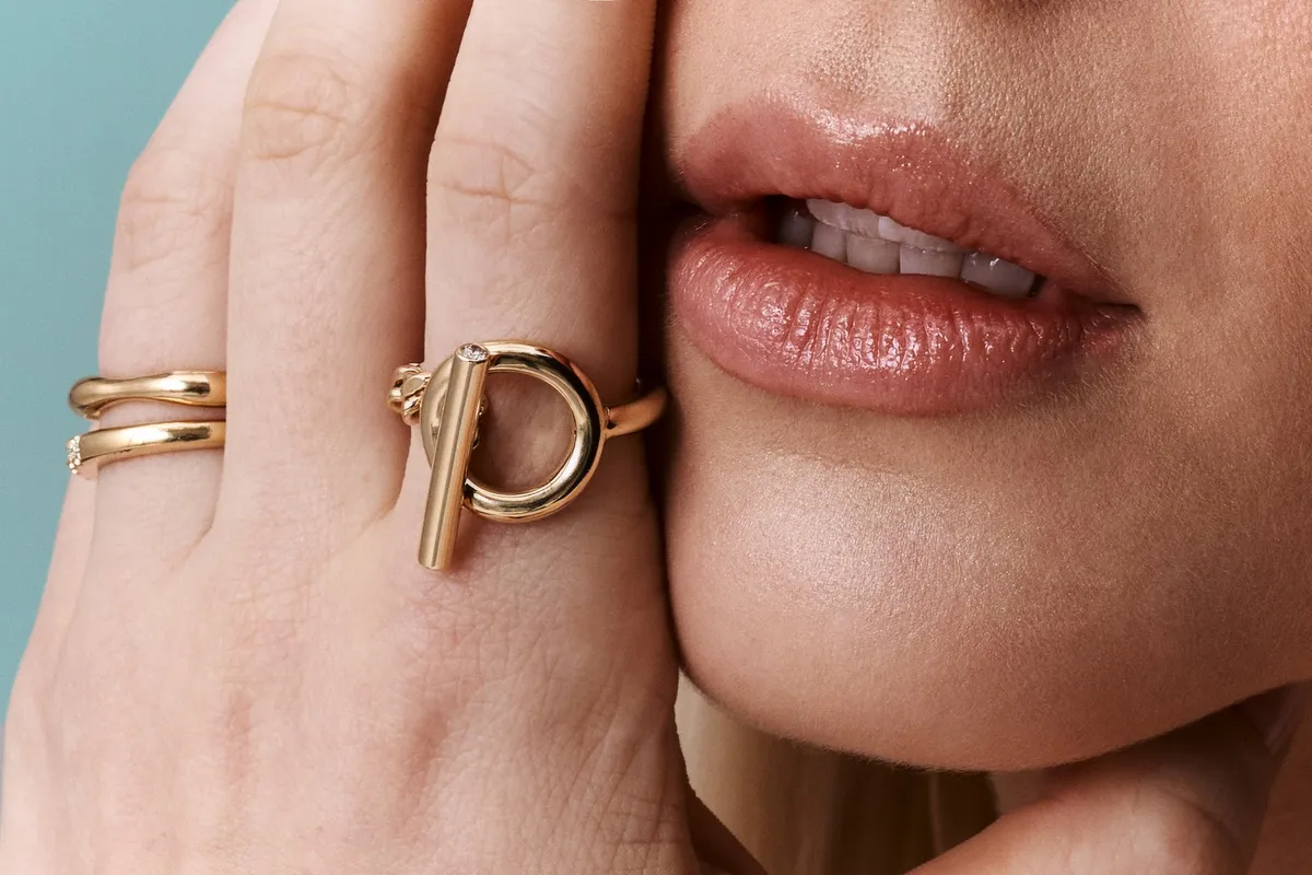 Monano, close-up of gold rings including a toggle-design ring on a hand beside the lips, jewellery campaign 2024, photographed by Kilian Amrehn