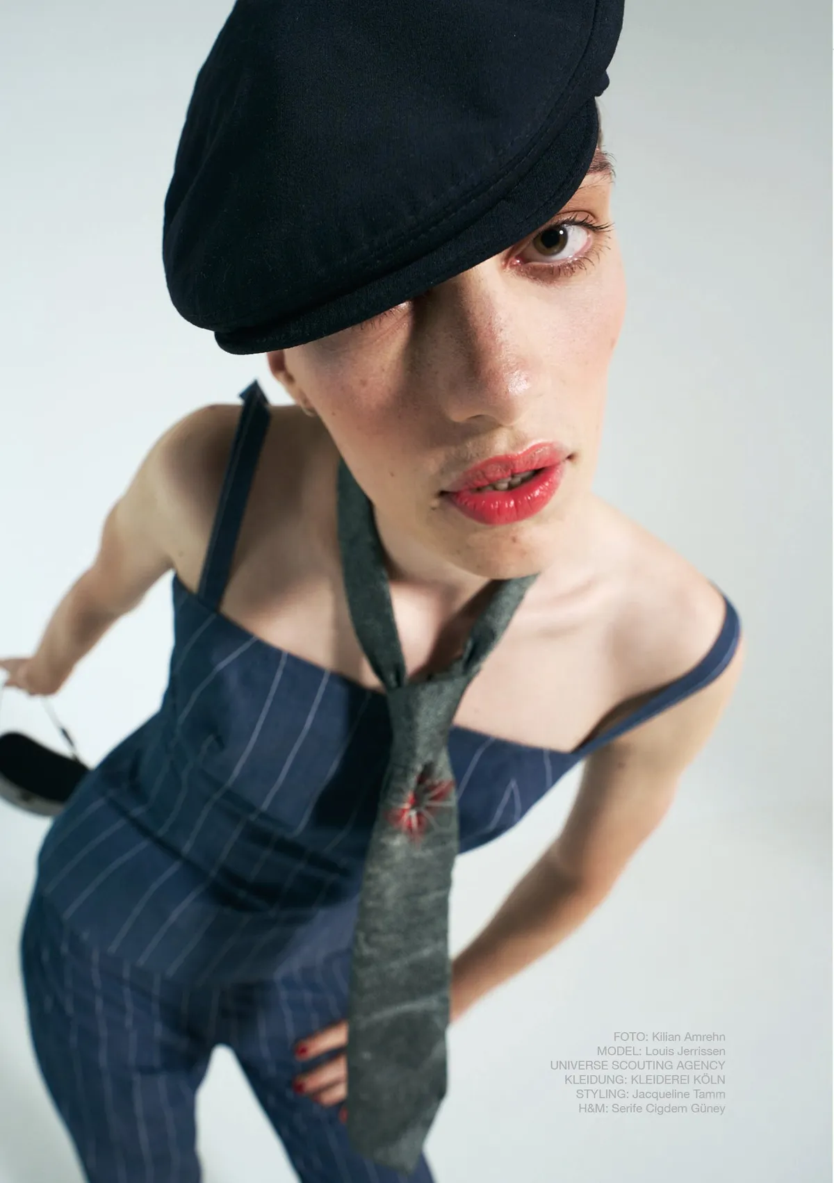 New Icons' Club Magazine, model in a black flat cap, red lipstick and pinstripe jumpsuit leaning toward the camera, issue 1 2023, photographed by Kilian Amrehn