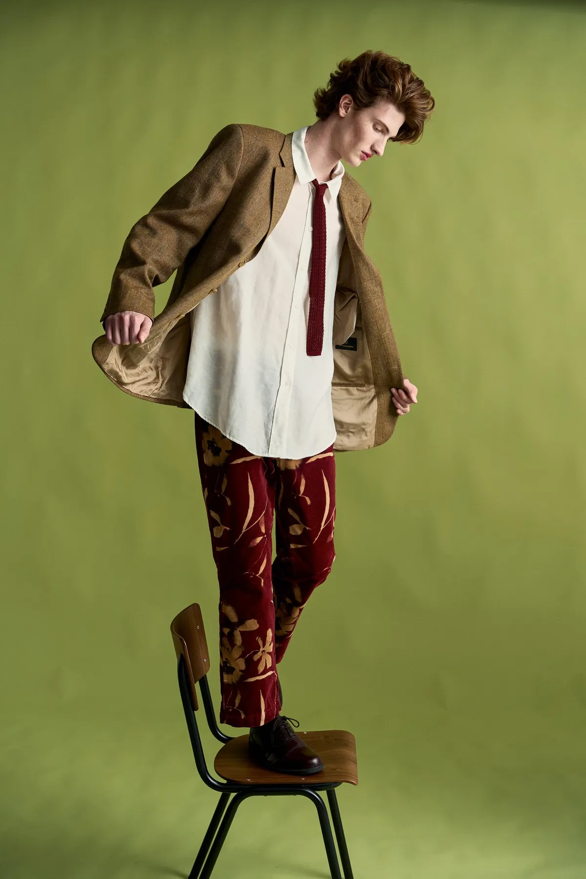 New Icons' Club Magazine, model in a tweed blazer standing with one foot on a wooden chair, opening the jacket, olive green, editorial 2nd Hand 2024, photographed by Kilian Amrehn