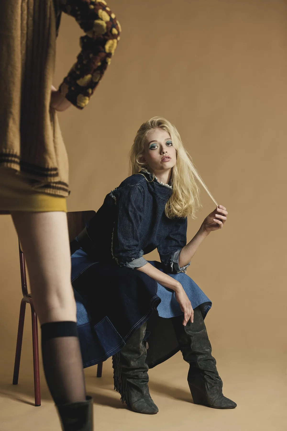 New Icons' Club Magazine, blonde model in a denim jacket and skirt with slouch boots on a chair, warm beige tones, editorial 2nd Hand 2024, photographed by Kilian Amrehn