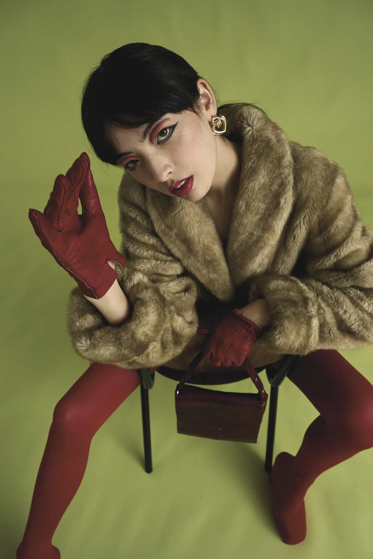 New Icons' Club Magazine, short-haired model with red eyeshadow in faux fur, red gloves and tights against olive green, editorial 2nd Hand 2024, photographed by Kilian Amrehn