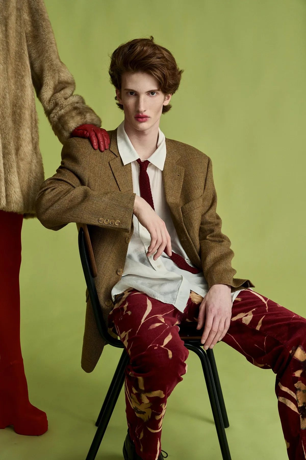 New Icons' Club Magazine, curly-haired model in a tweed blazer, red tie and patterned velvet trousers on a chair against olive green, editorial 2nd Hand 2024, photographed by Kilian Amrehn