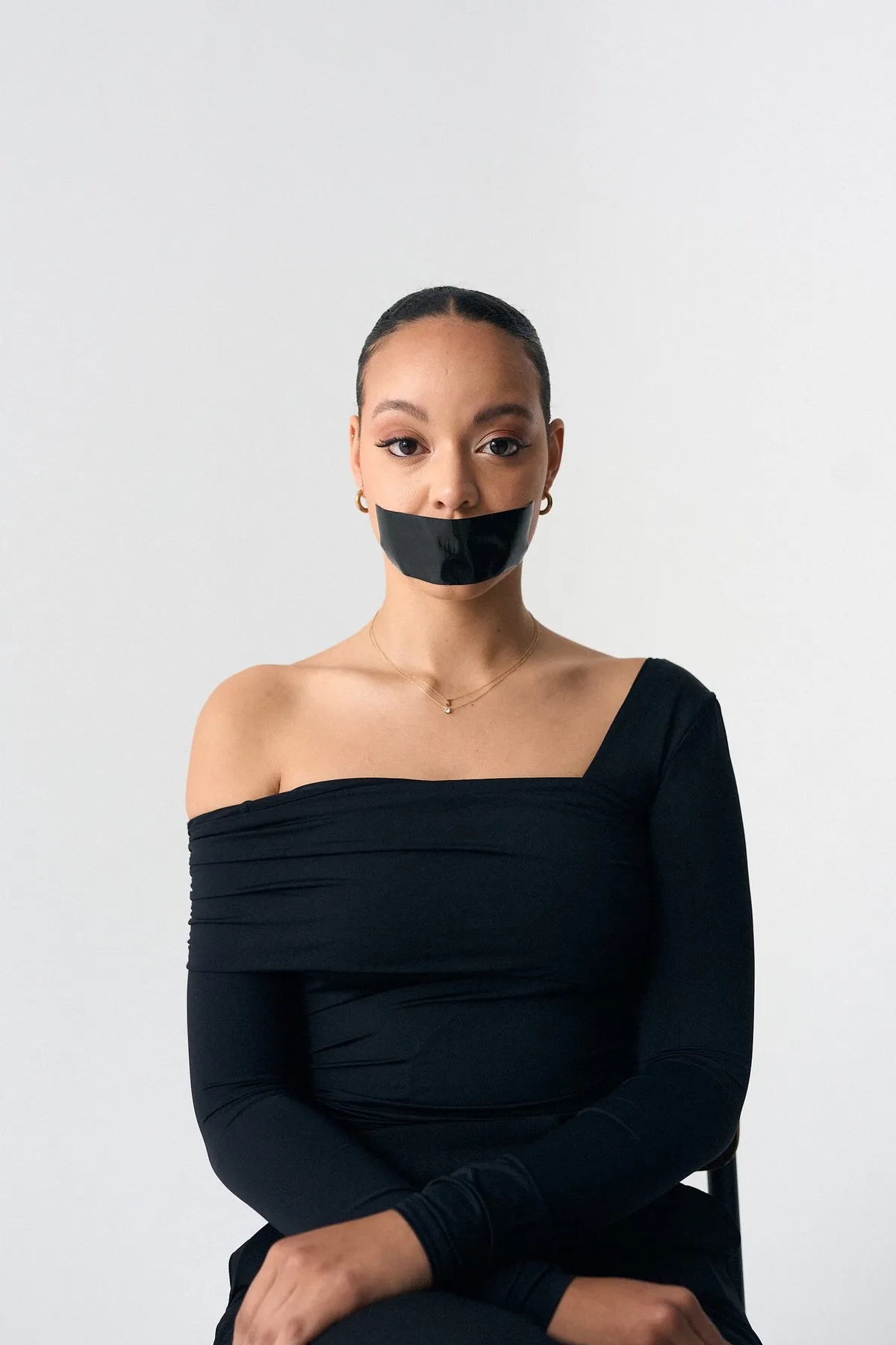 #niewiederleise, Frau mit zurückgebundenem Haar im schwarzen One-Shoulder-Top, Mund mit schwarzem Klebeband verschlossen, Kampagne 2024, fotografiert von Kilian Amrehn