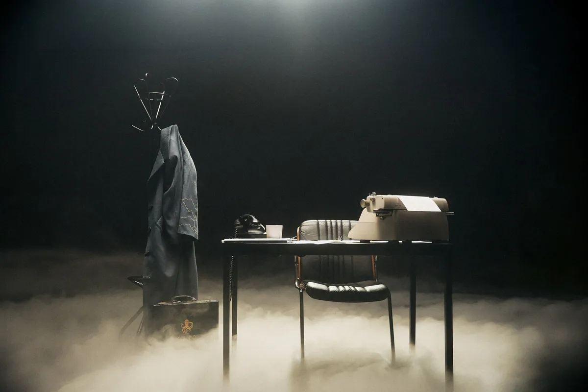 Ozean der Stille, leerer Schreibtisch mit Schreibmaschine, Telefon und Garderobe mit Mantel im Bodennebel, dunkles Spotlicht, Modestrecke 2026, fotografiert von Kilian Amrehn