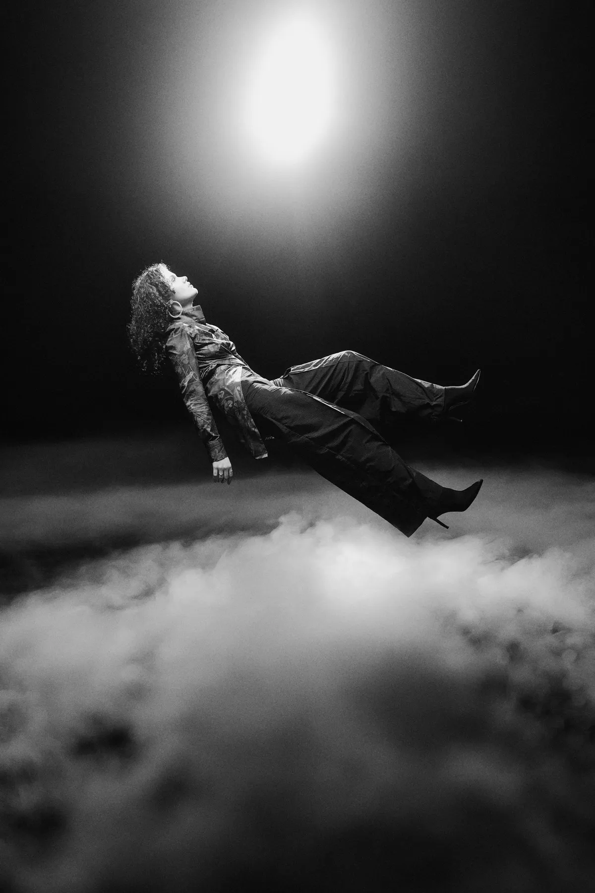 Ozean der Stille, Model schwebt waagerecht über einer Nebelwolke unter einem hellen Lichtkegel, Schwarzweiß, Modestrecke 2026, fotografiert von Kilian Amrehn