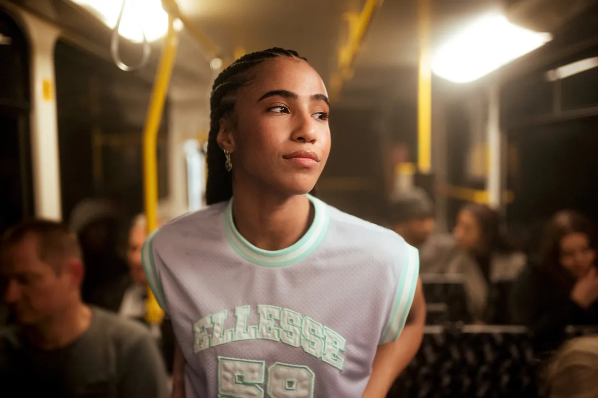Peek & Cloppenburg x Ellesse, model with braids in a pale Ellesse mesh jersey inside a tram at night, warm light, campaign 2022, photographed by Kilian Amrehn