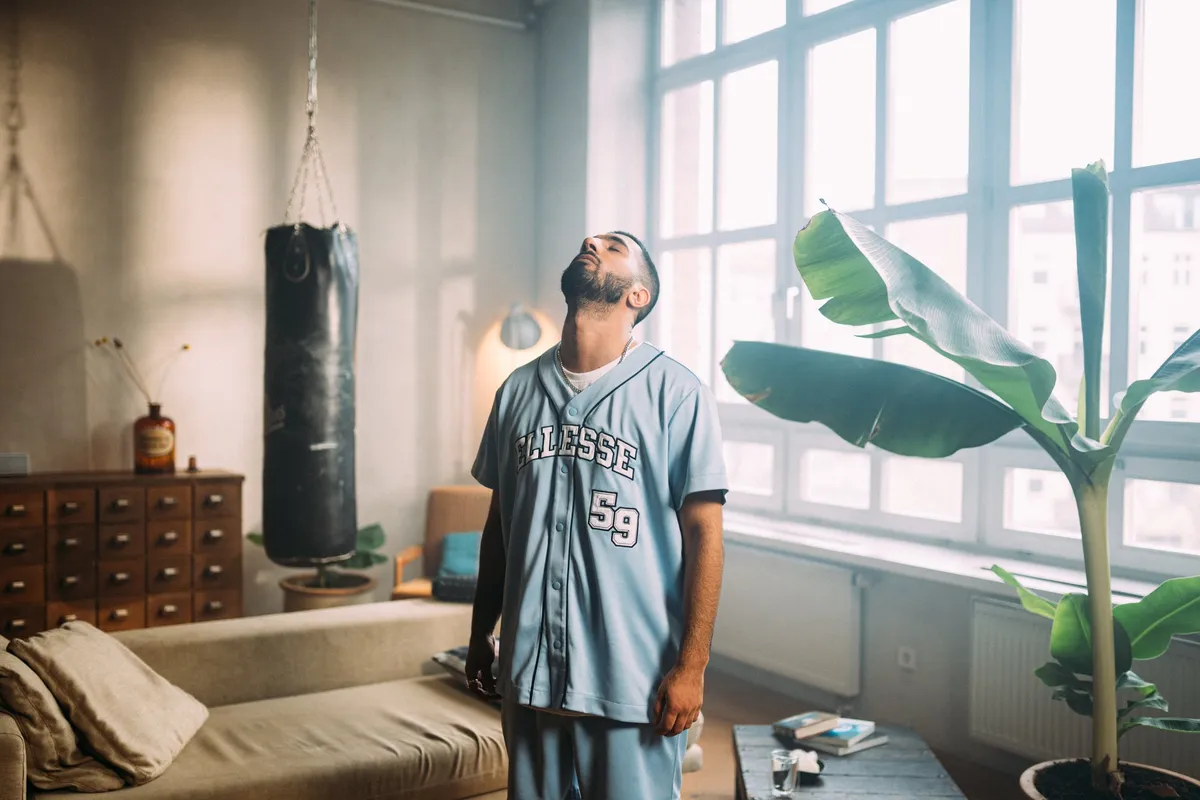 Peek & Cloppenburg x Ellesse, Model im hellblauen Baseball-Shirt mit Ellesse-Schriftzug in einem Loft mit Boxsack und Bananenpflanze, Kampagne 2022, fotografiert von Kilian Amrehn