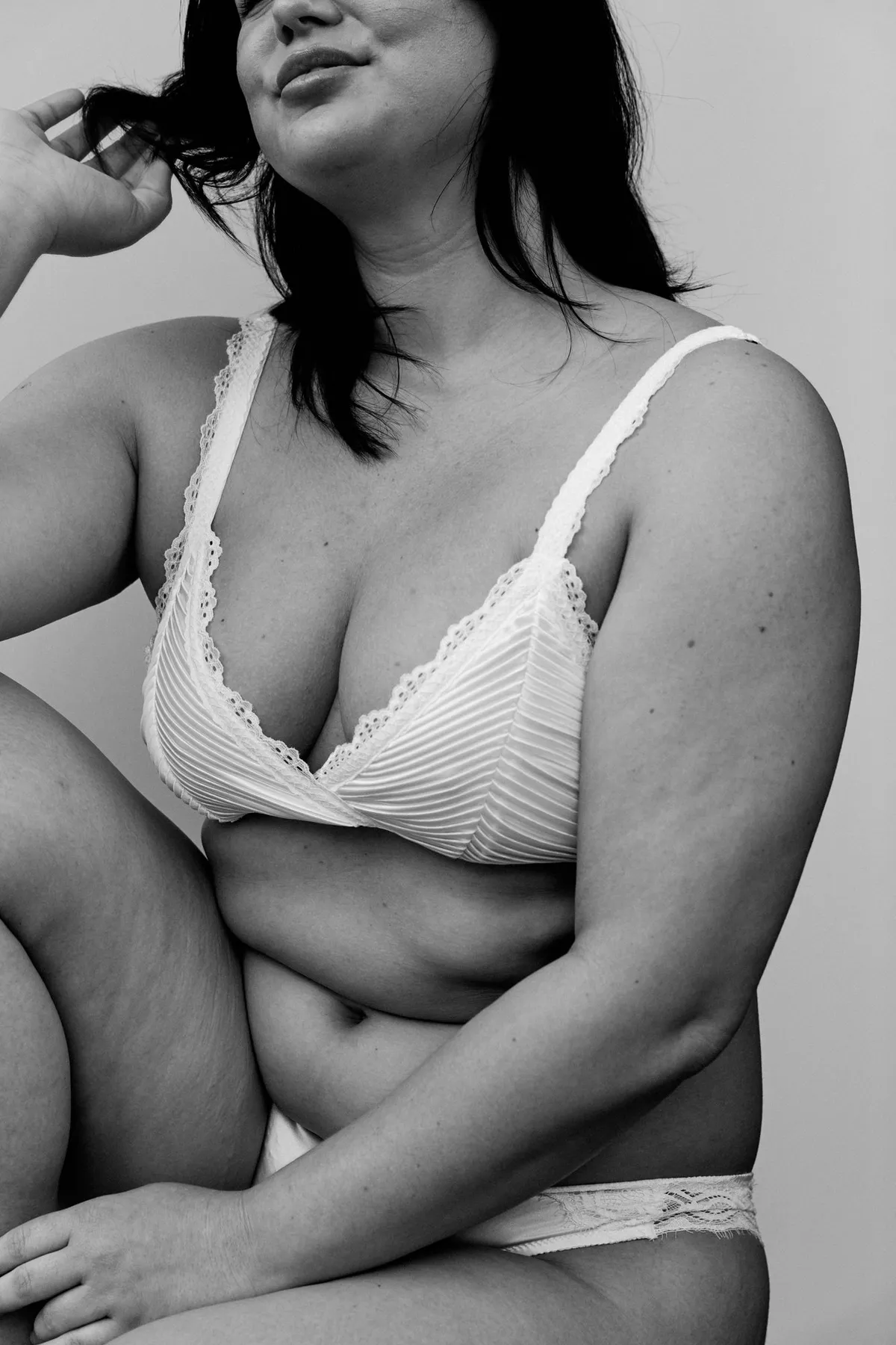 Phiala, dark-haired model in a white pleated lace bra, natural curves, relaxed pose in black and white, campaign 2024, photographed by Kilian Amrehn