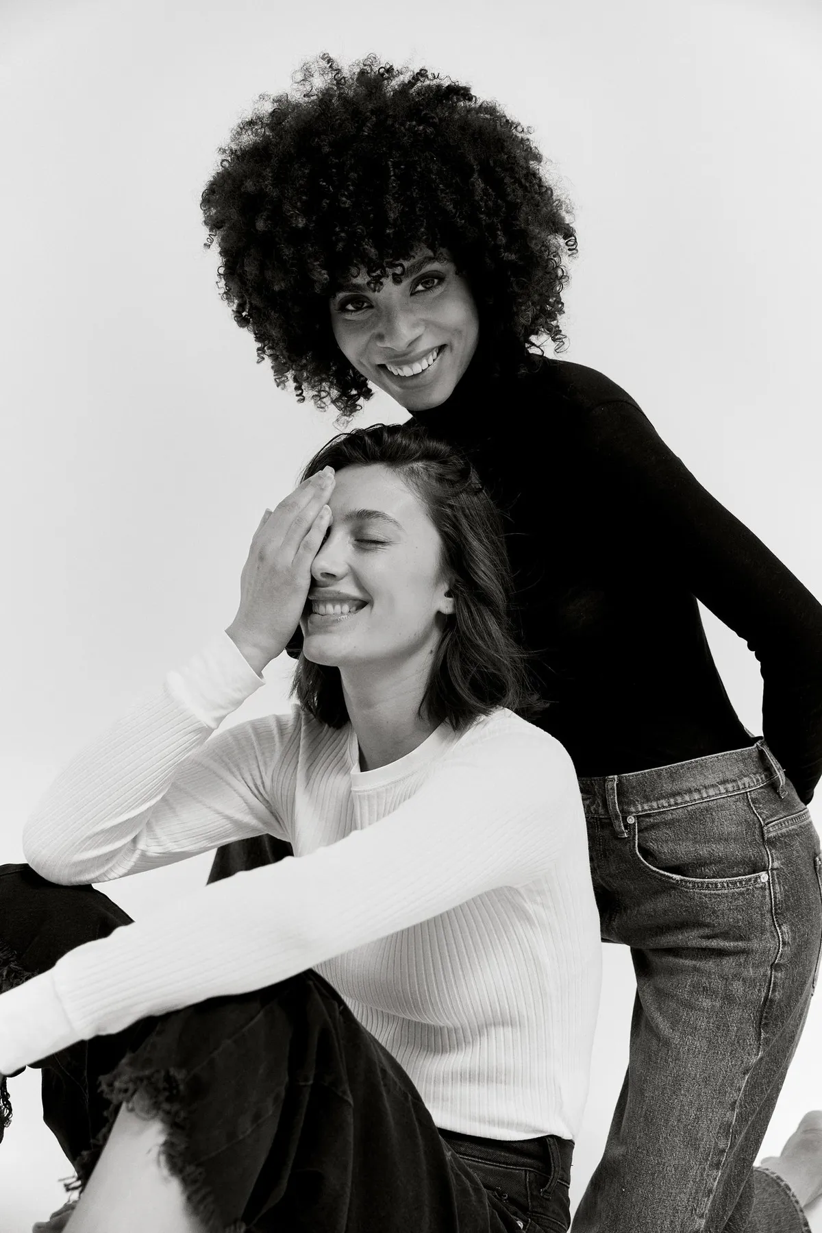 PNTS, two laughing models in jeans and ribbed tops, one covering an eye with her hand, black and white, campaign 2022, photographed by Kilian Amrehn