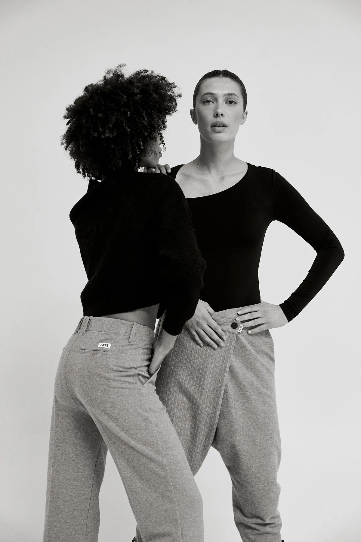 PNTS, two models in black tops and grey trousers standing close together, black and white, campaign 2022, photographed by Kilian Amrehn