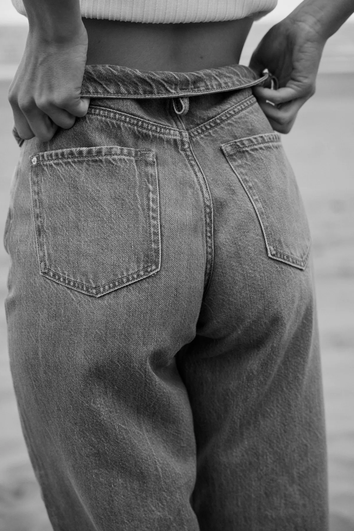 PNTS, hands adjusting the waistband of grey jeans from behind, back pocket detail in black and white, Noordwijk 2023, photographed by Kilian Amrehn