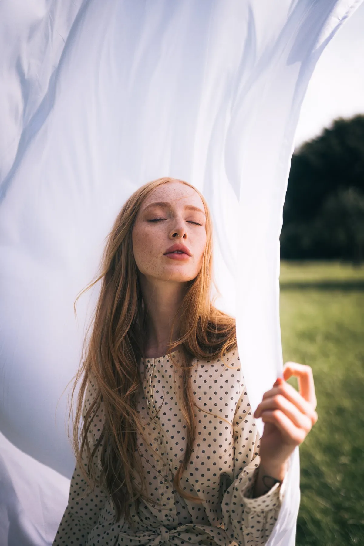 Rock Fairyland, red-haired model with freckles in a polka dot dress against a billowing white sheet in a meadow, editorial 2021, photographed by Kilian Amrehn