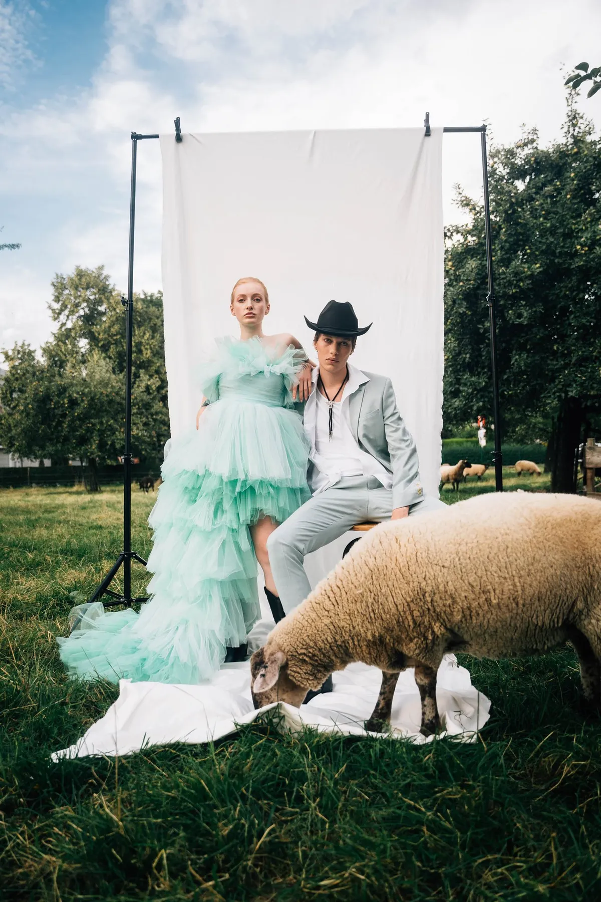Rock Fairyland, model in a mint tulle gown and model in a cowboy hat before a white backdrop on a sheep pasture, editorial 2021, photographed by Kilian Amrehn