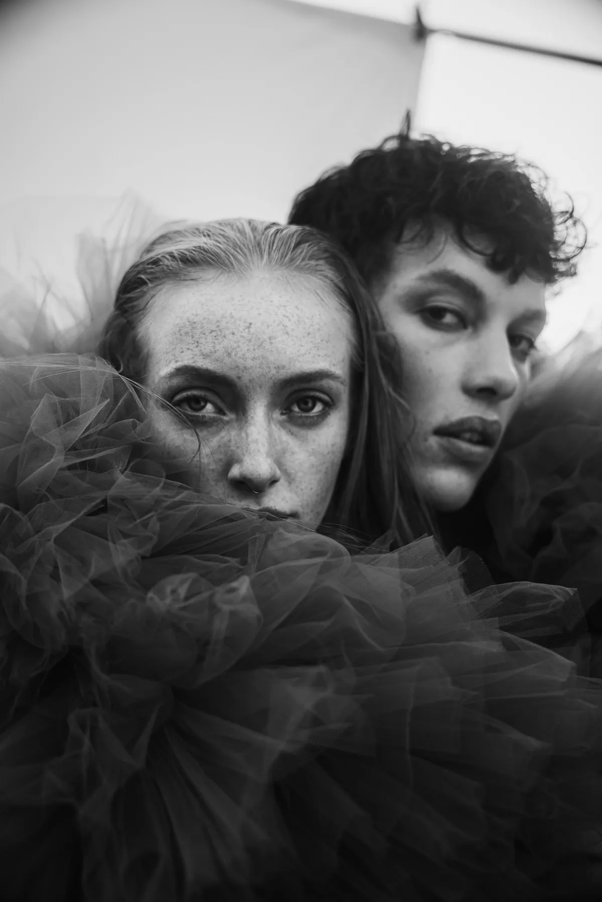 Rock Fairyland, two faces side by side wrapped in dark tulle, freckled model looking straight at camera, black and white portrait, editorial 2021, photographed by Kilian Amrehn