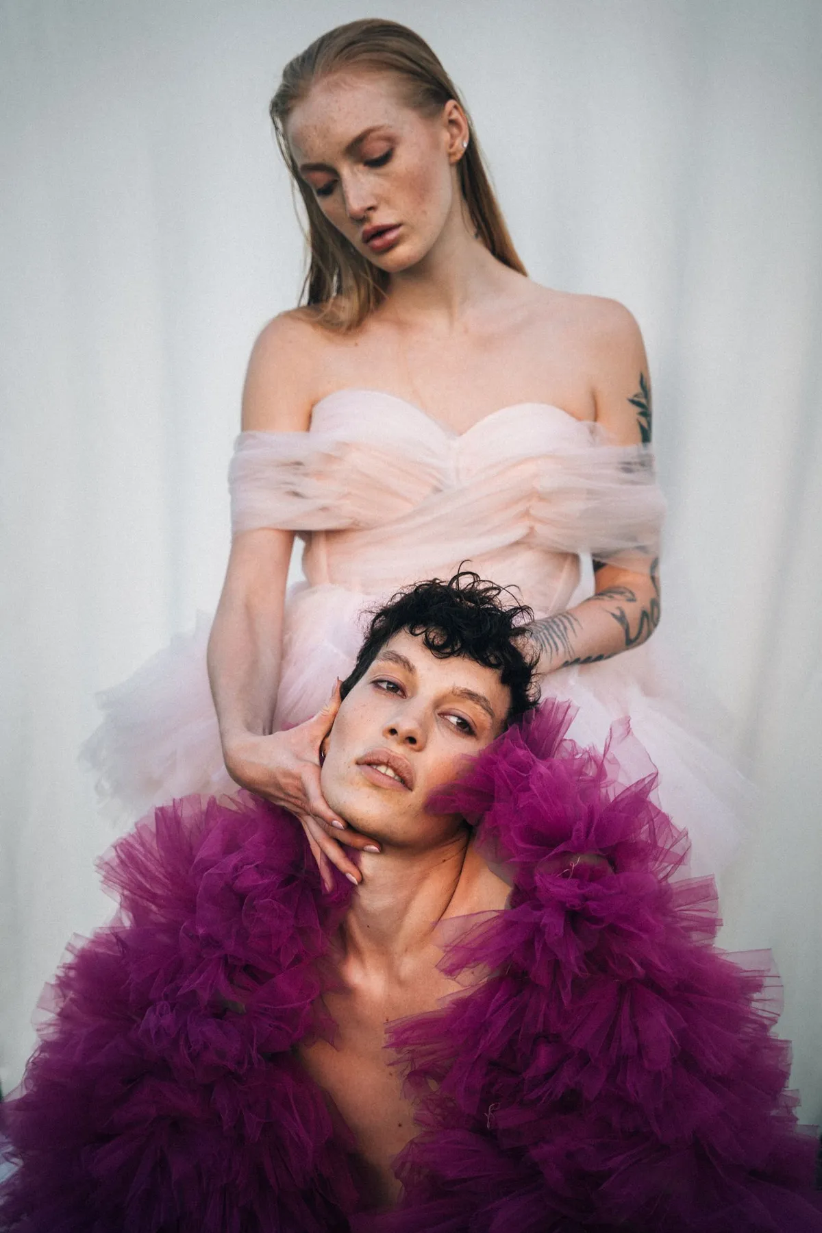 Rock Fairyland, model in a pale pink off-shoulder dress cradling the face of a model in magenta tulle, soft backdrop, editorial 2021, photographed by Kilian Amrehn