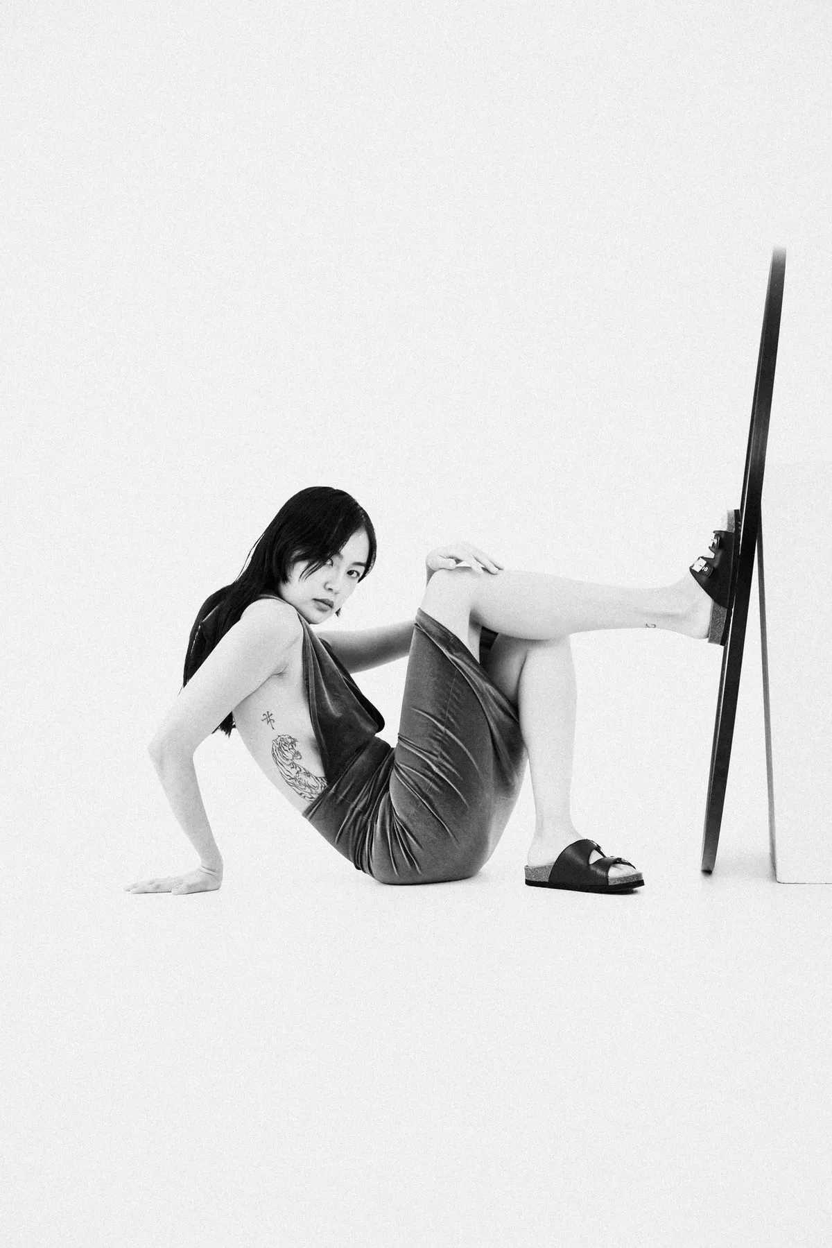Scholl iconic, model in black sandals sitting on the floor with a foot against a standing mirror, black and white, campaign October 2021, photographed by Kilian Amrehn