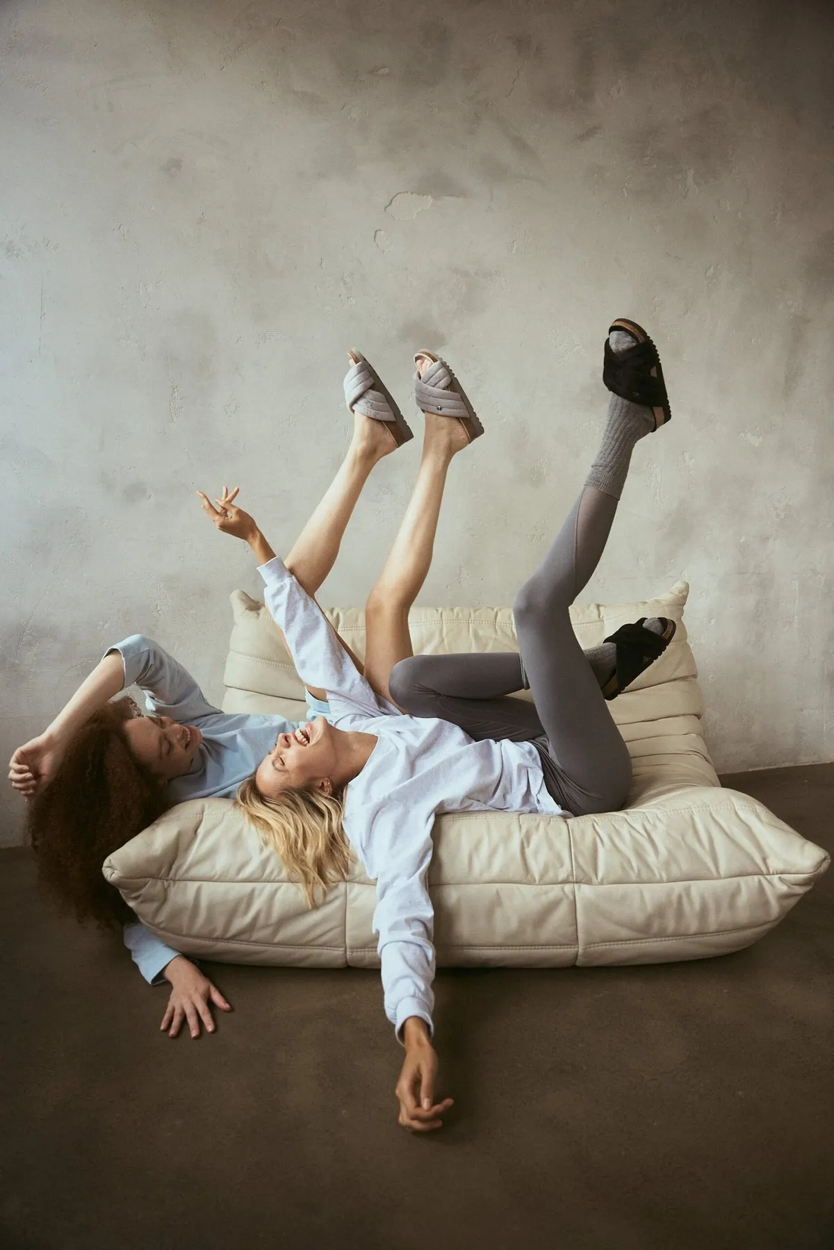 Scholl Comfort, two models lying back on a lounge cushion kicking their legs up in slippers, studio July 2022, photographed by Kilian Amrehn