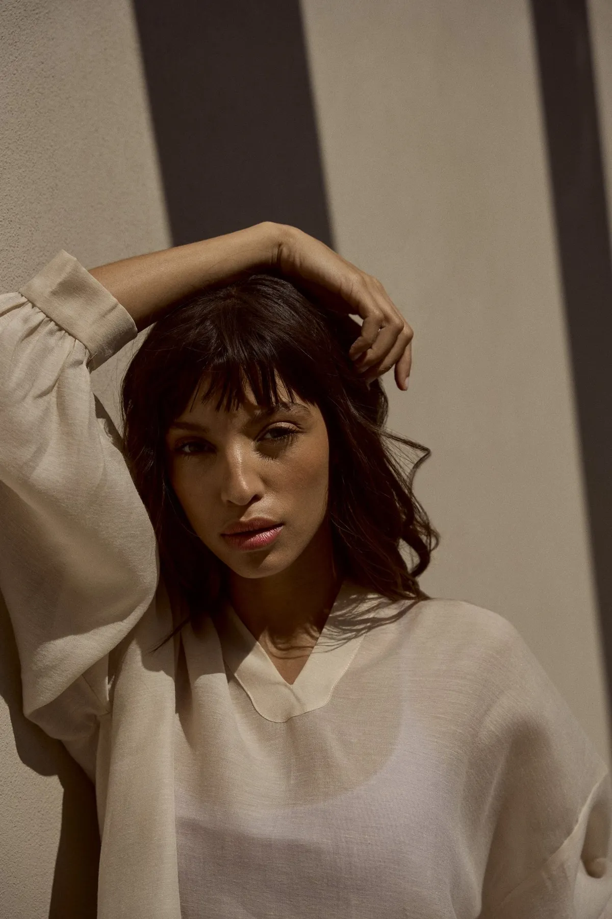 Scholl Comfort, model with bangs and hand in her hair in a sheer linen blouse, warm sunlight and shadow, Egypt 2023, photographed by Kilian Amrehn