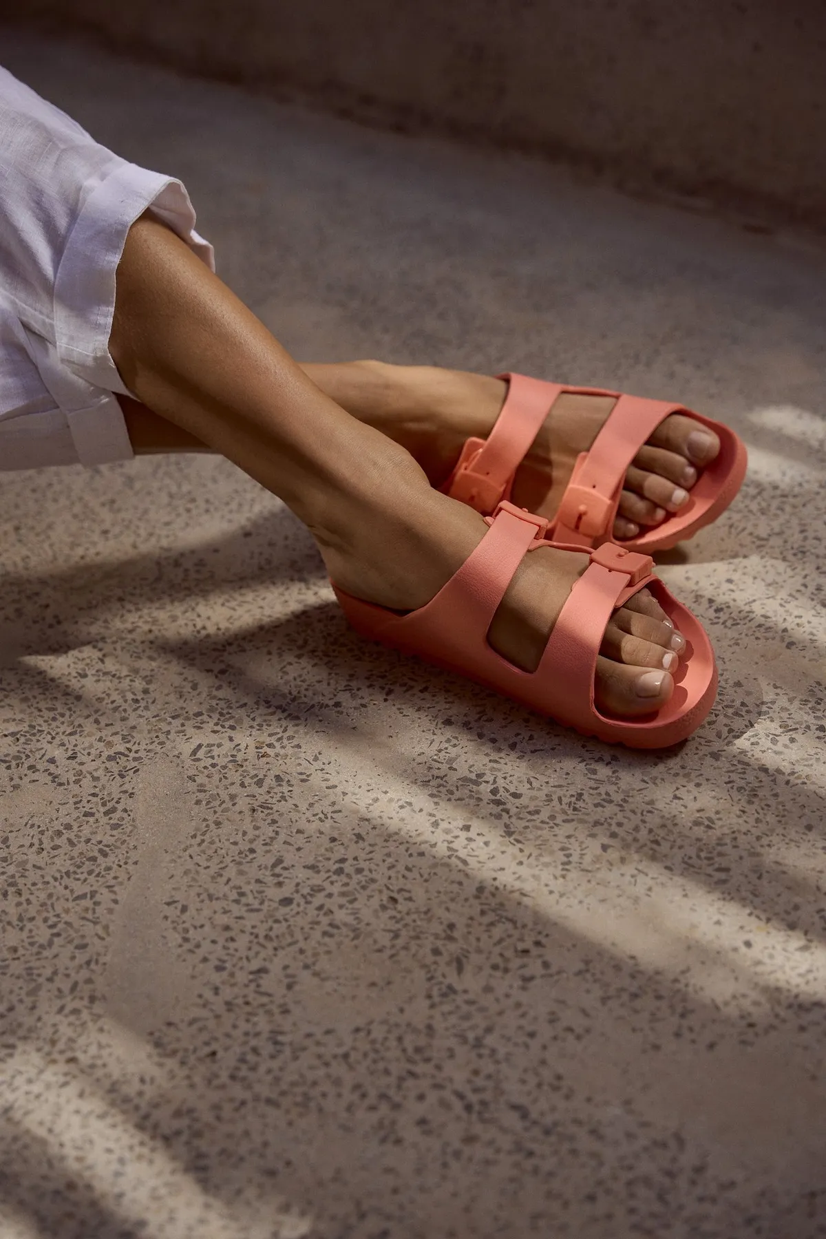 Scholl Comfort, crossed feet in salmon two-strap sandals on a terrazzo floor in sunlight, Egypt 2023, photographed by Kilian Amrehn