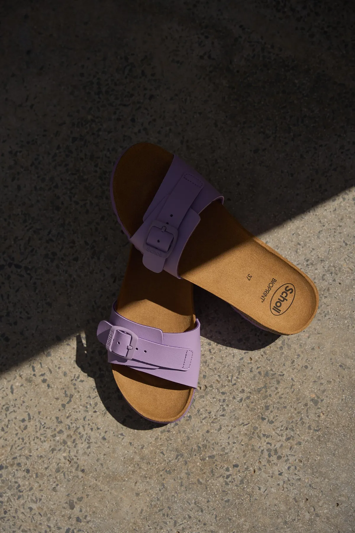 Scholl Comfort, lilac suede slides with buckle and cork footbed on a stone floor in hard light, Egypt 2023, photographed by Kilian Amrehn