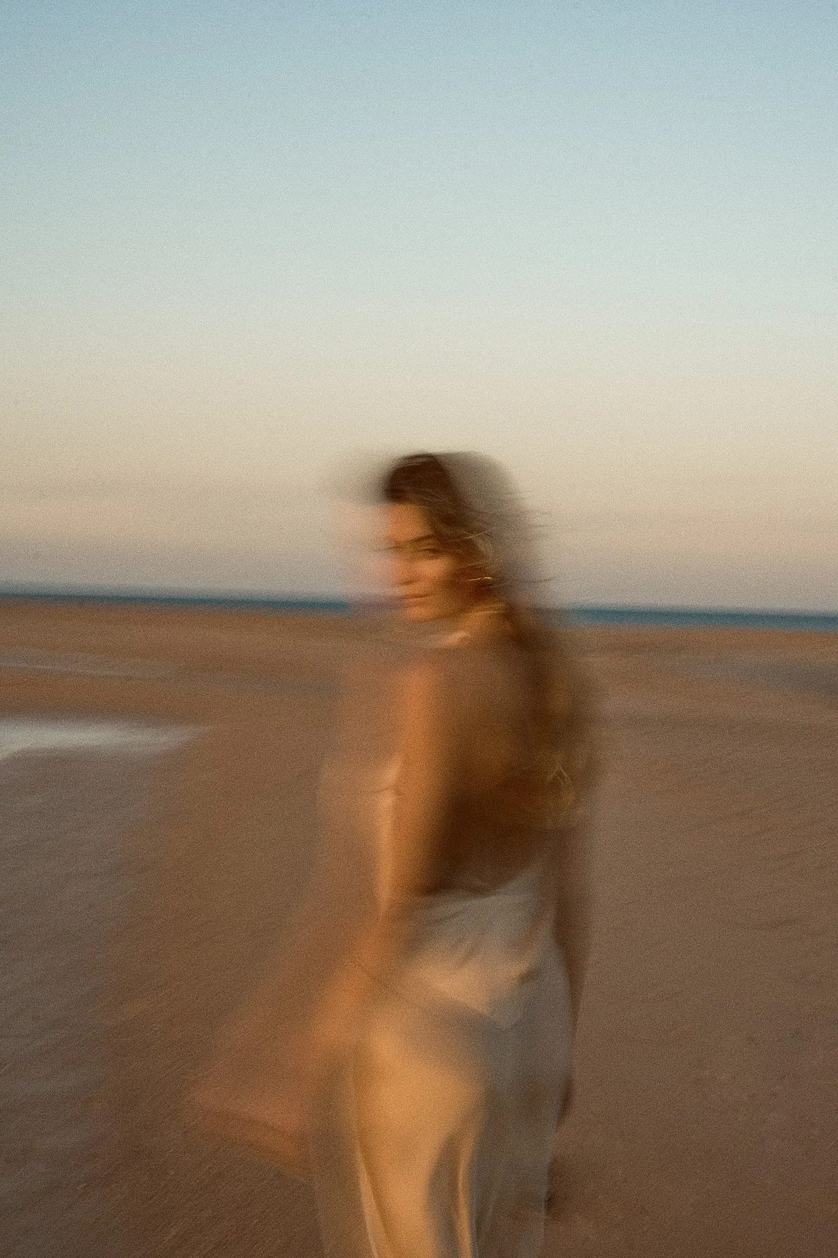 Scholl Comfort, model in a pale satin dress on the beach in motion blur, pastel evening sky, Egypt 2023, photographed by Kilian Amrehn