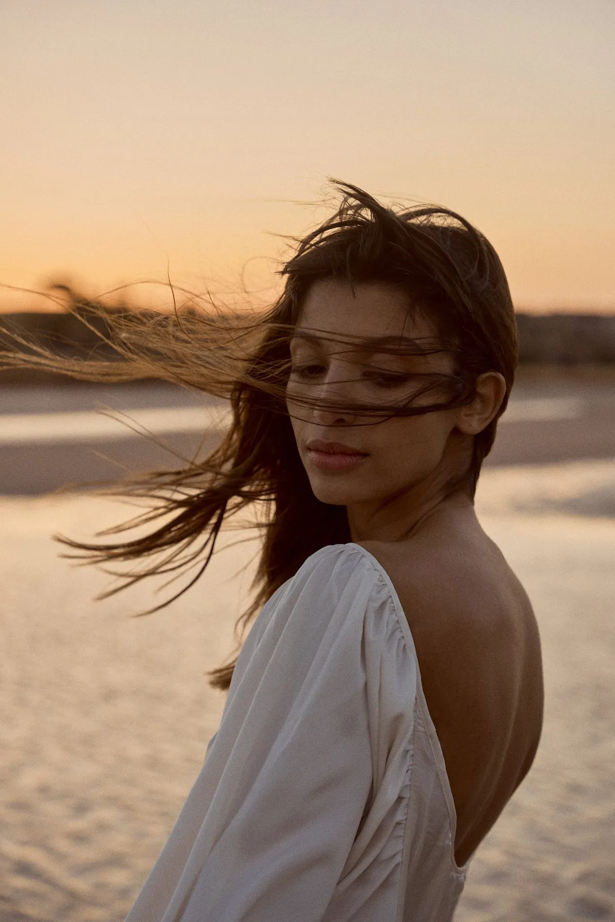 Scholl Comfort, model with wind-blown hair in a backless white dress, golden evening light on the beach, Egypt 2023, photographed by Kilian Amrehn