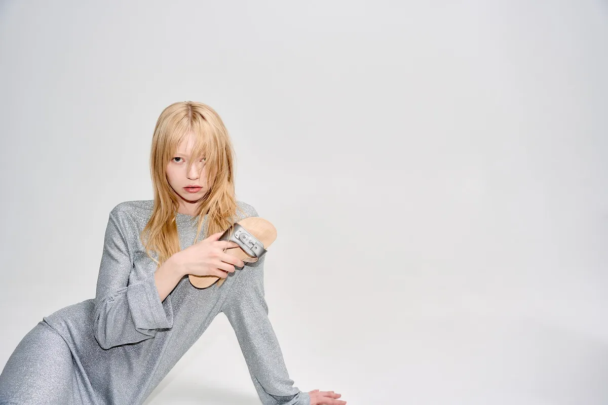 Scholl iconic, blonde model in a silver glitter dress holding a silver slide, light studio background, campaign February 2023, photographed by Kilian Amrehn