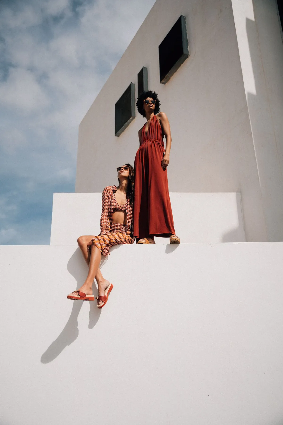 Scholl iconic, two models in red and terracotta with sandals on white architecture against the sky, campaign Fuerteventura 2021, photographed by Kilian Amrehn