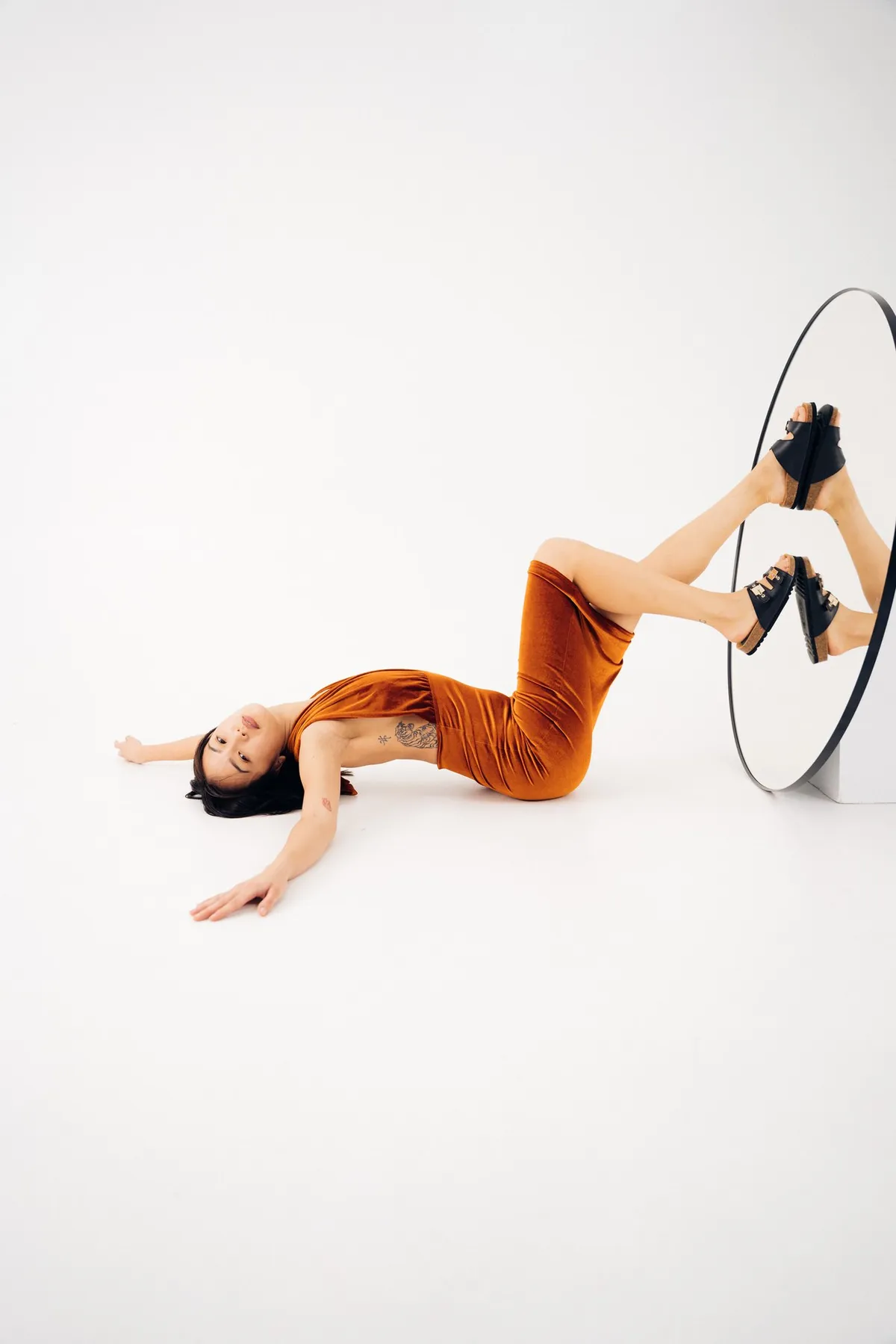 Scholl iconic, model in a rust dress lying on the floor, feet in black sandals reflected in a round mirror, campaign October 2021, photographed by Kilian Amrehn