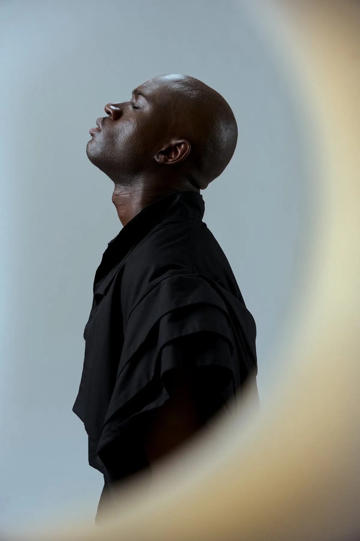 JEREMIAH Silent Escape, model in a black shirt in profile with eyes closed, framed through a round opening, campaign 2024, photographed by Kilian Amrehn