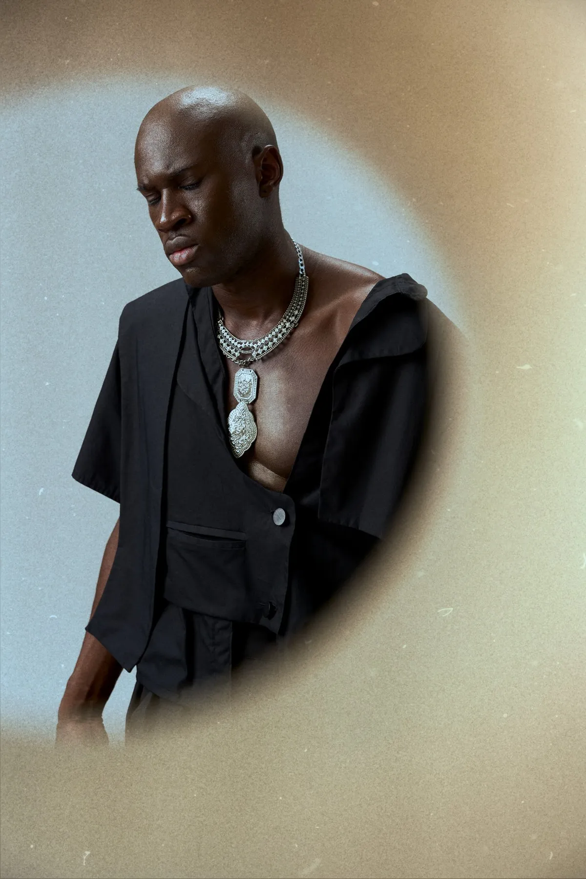 JEREMIAH Silent Escape, bald model in an open black shirt and silver chain looking down, oval framing, campaign 2024, photographed by Kilian Amrehn