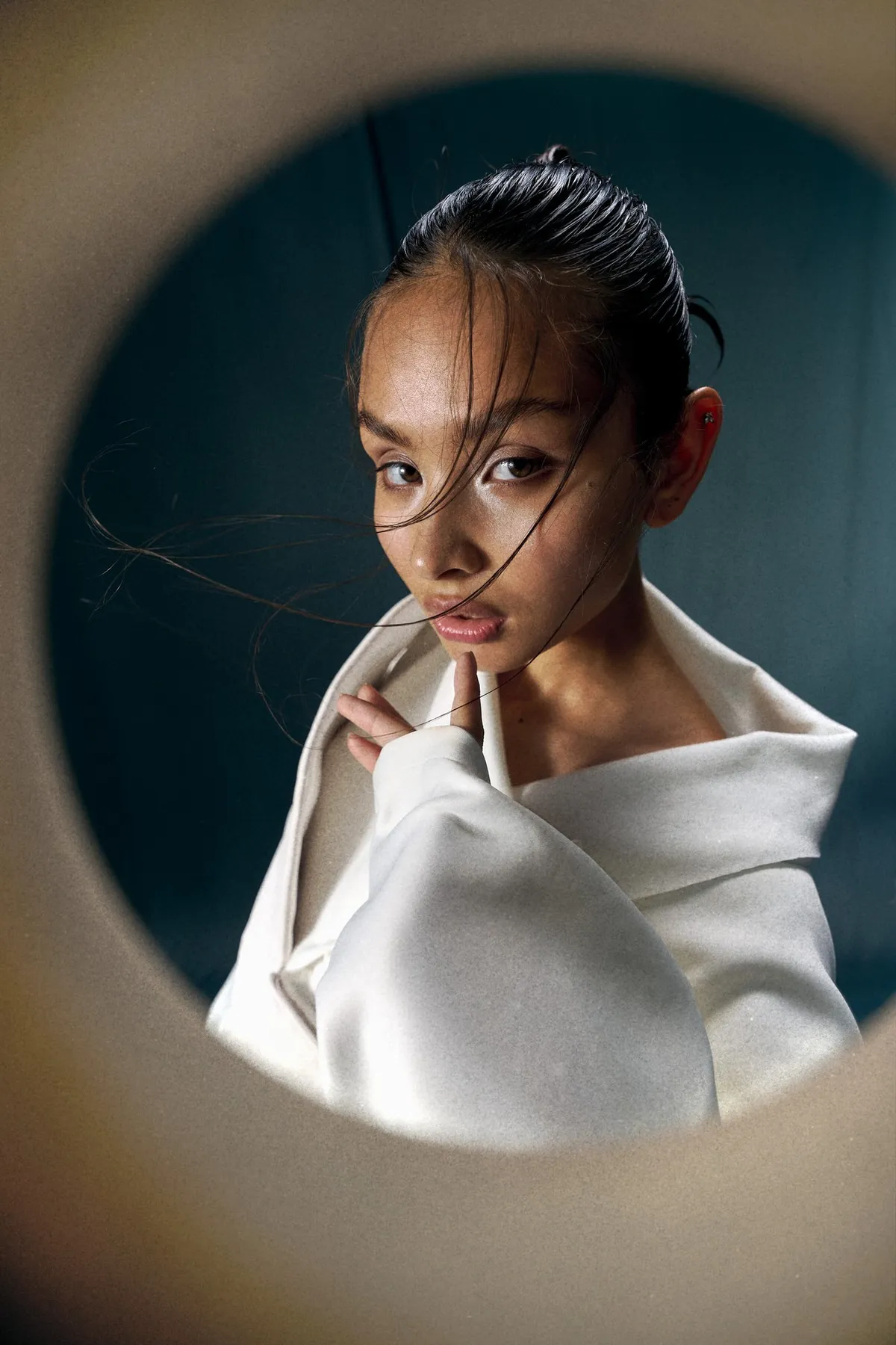 JEREMIAH Silent Escape, close-up of a model with loose strands across the face in a white jacket, finger at chin, round frame, campaign 2024, photographed by Kilian Amrehn