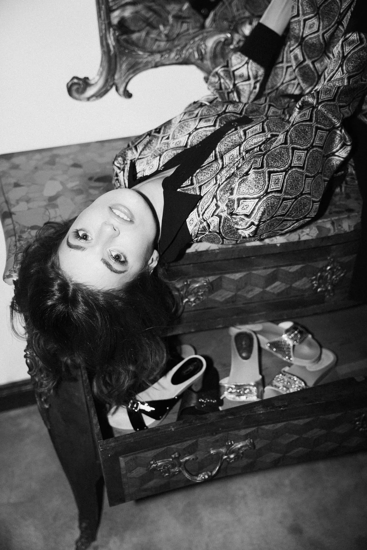 The Wants, model lying upside down on a dresser with drawers full of clogs, patterned satin suit in black and white, campaign 2020, photographed by Kilian Amrehn