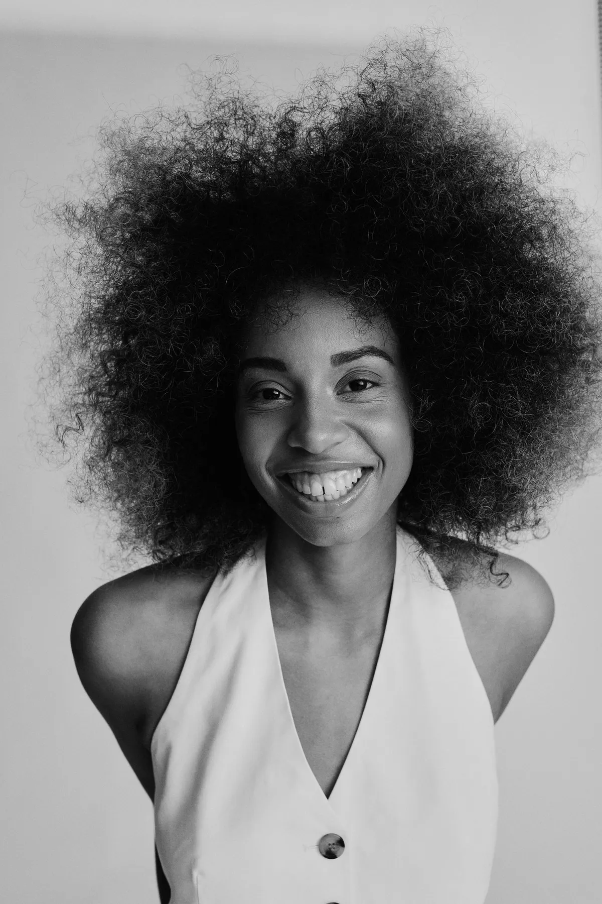 Reflections of Identity, lachendes Model mit großem Afro im weißen Neckholder-Top, Schwarzweiß-Porträt, Porträtserie 2024, fotografiert von Kilian Amrehn