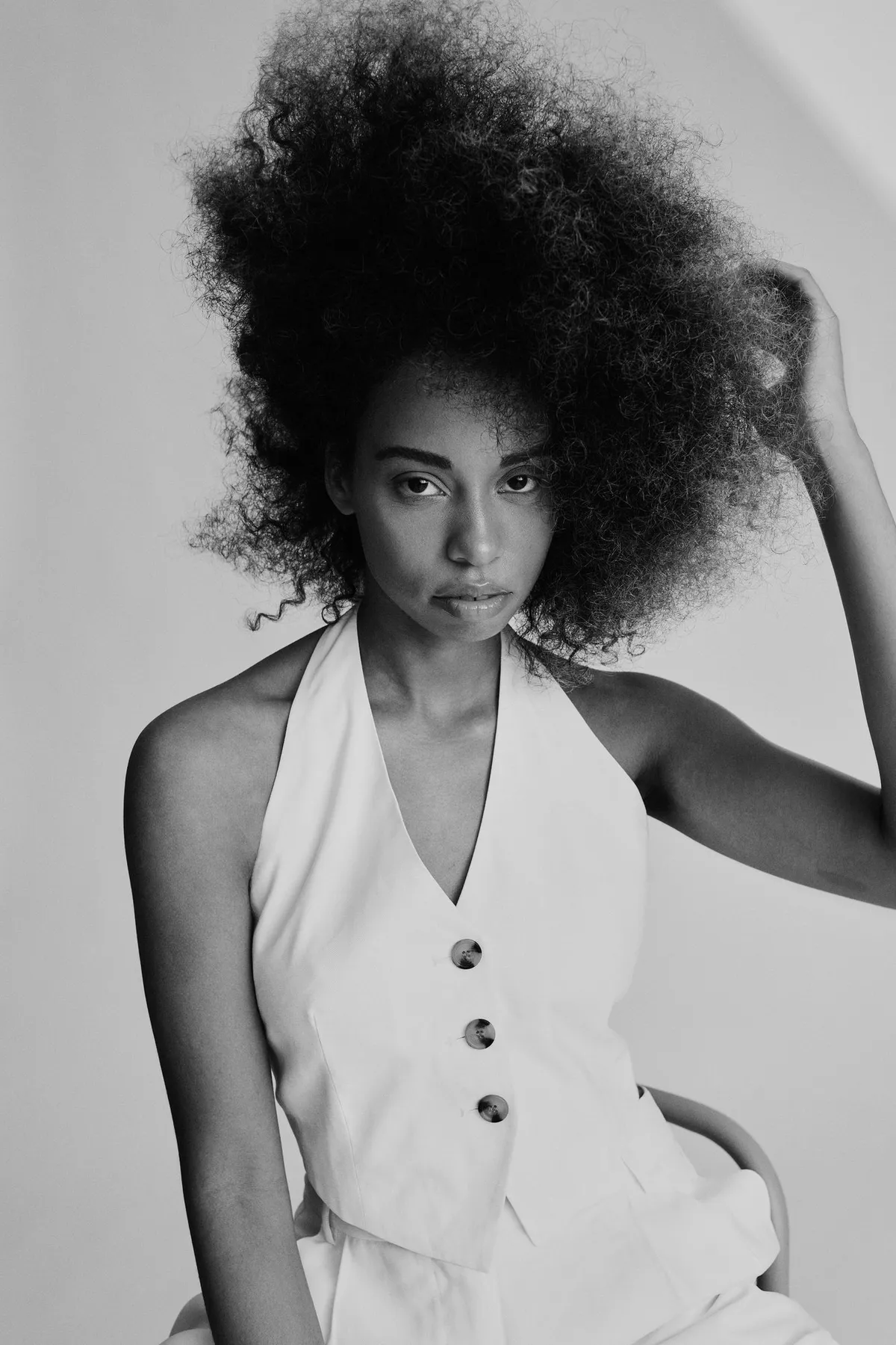 Reflections of Identity, model with an afro in a white waistcoat touching her hair, calm gaze, black and white, portrait series 2024, photographed by Kilian Amrehn