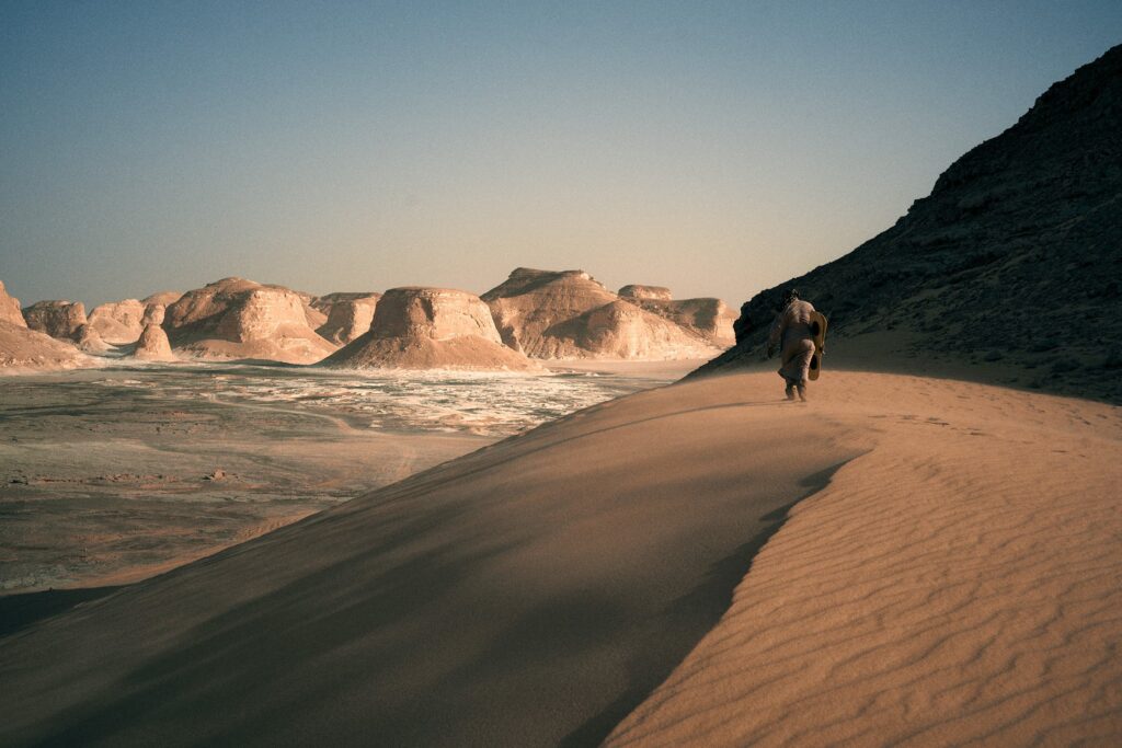 Foto von einer Person auf einer Sanddüne in einer Wüstenlandschaft mit Felsen