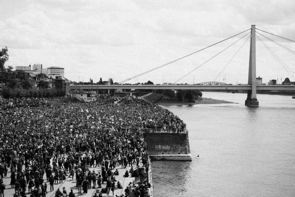 Schwarz-Weiß Aufnahme von einer BlackLivesMatter Demo am Rand von einem Fluss an einer Brücke