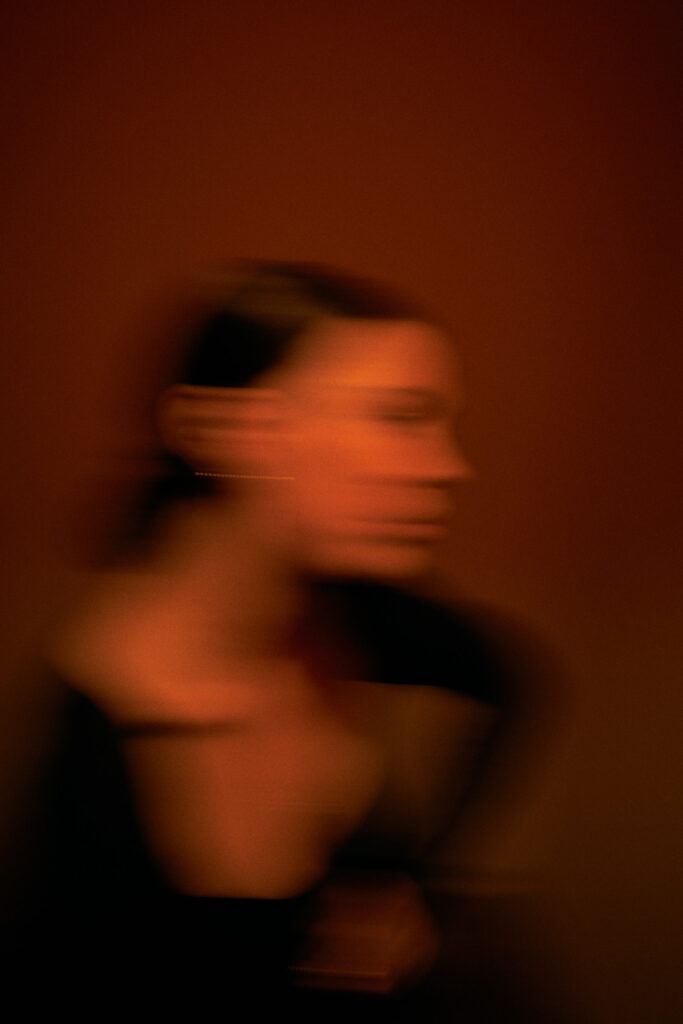 Porträt einer Frau in Bewegung mit verschwommenen Konturen vor rotbraunem Hintergrund